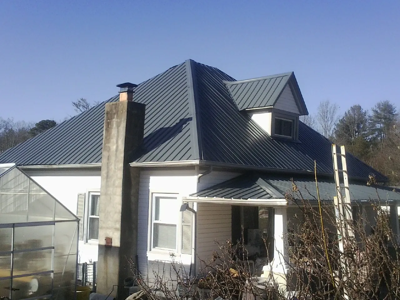Dark blue standing seam metal roof on a white farmhouse with dormer — Slate & Tile Roof Repair by Roofing Brothers in New City