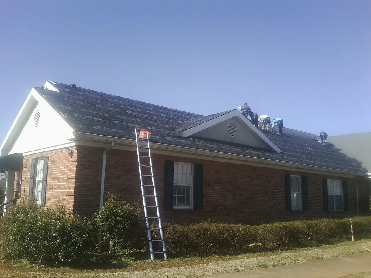Crew tearing shingles off a brick ranch roof with a ladder set — Metal Roof Repair work by our crew in New City