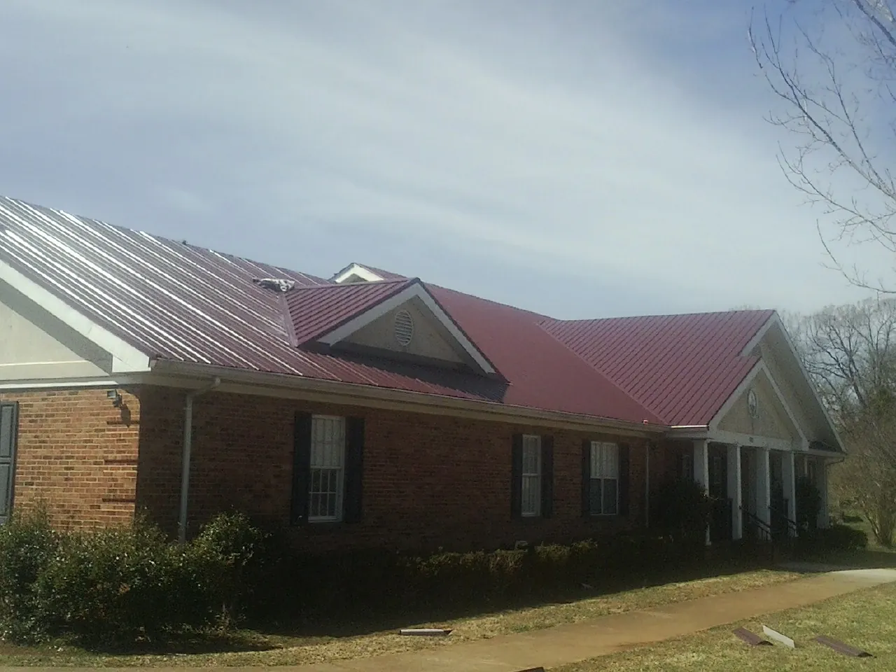 Red metal roof with gabled entries on a long brick building, from a Hail Damage Roof Repair job in New City