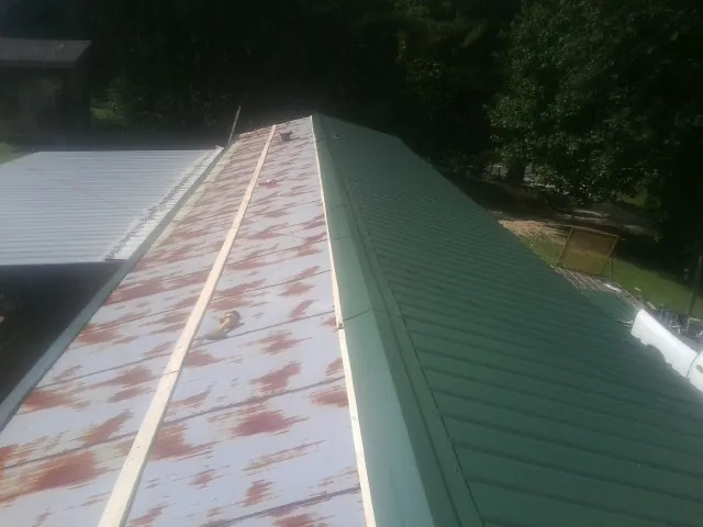 Old rusted panels beside newly installed green metal roofing — Wind Damage Roof Repair by Roofing Brothers in New City