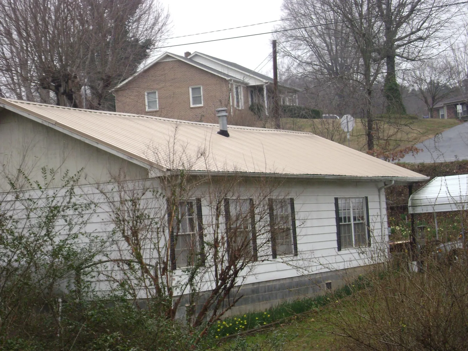 Tan metal roof on a white sided house set into a hillside — Commercial Roofing by Roofing Brothers in New City